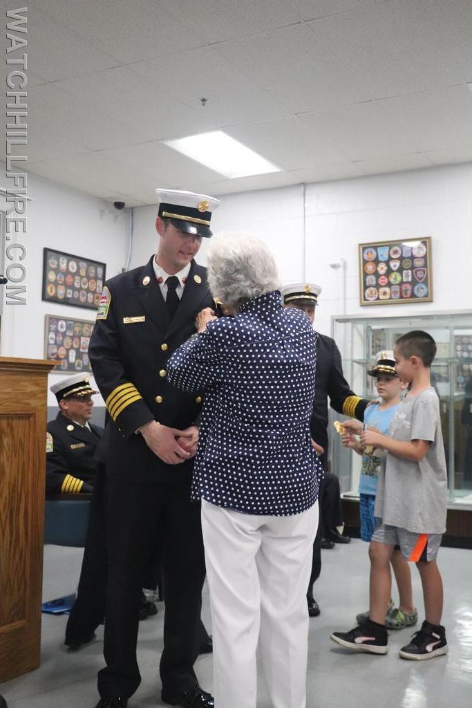 Mrs. Cugini pins on her Grandson's badge. She is the Daughter of Ashaway's First Fire Chief, G. Byron Champlin